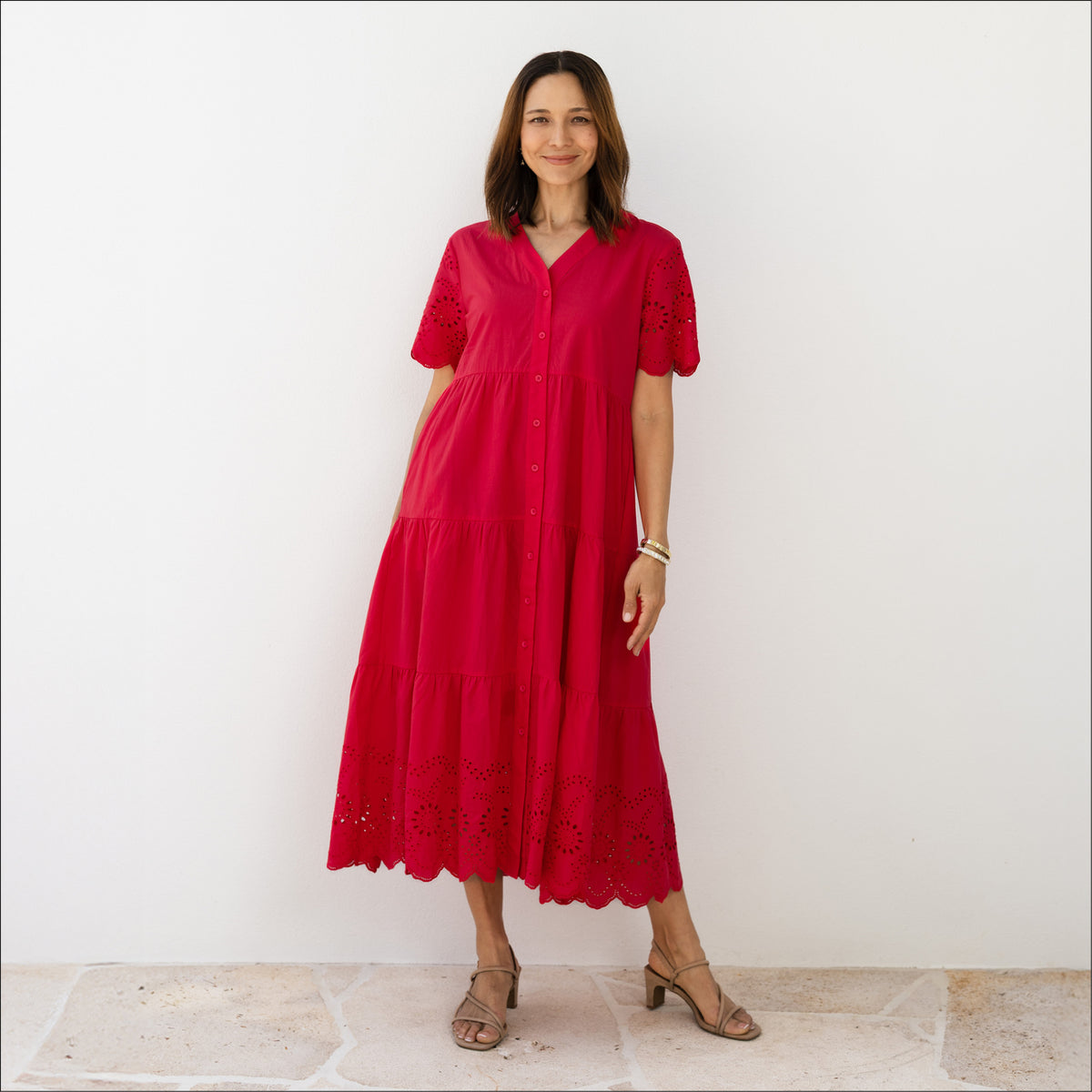 Brunette woman in a tiered red V-neck sleeved dress with a button-down front and broderie anglaise hemline.