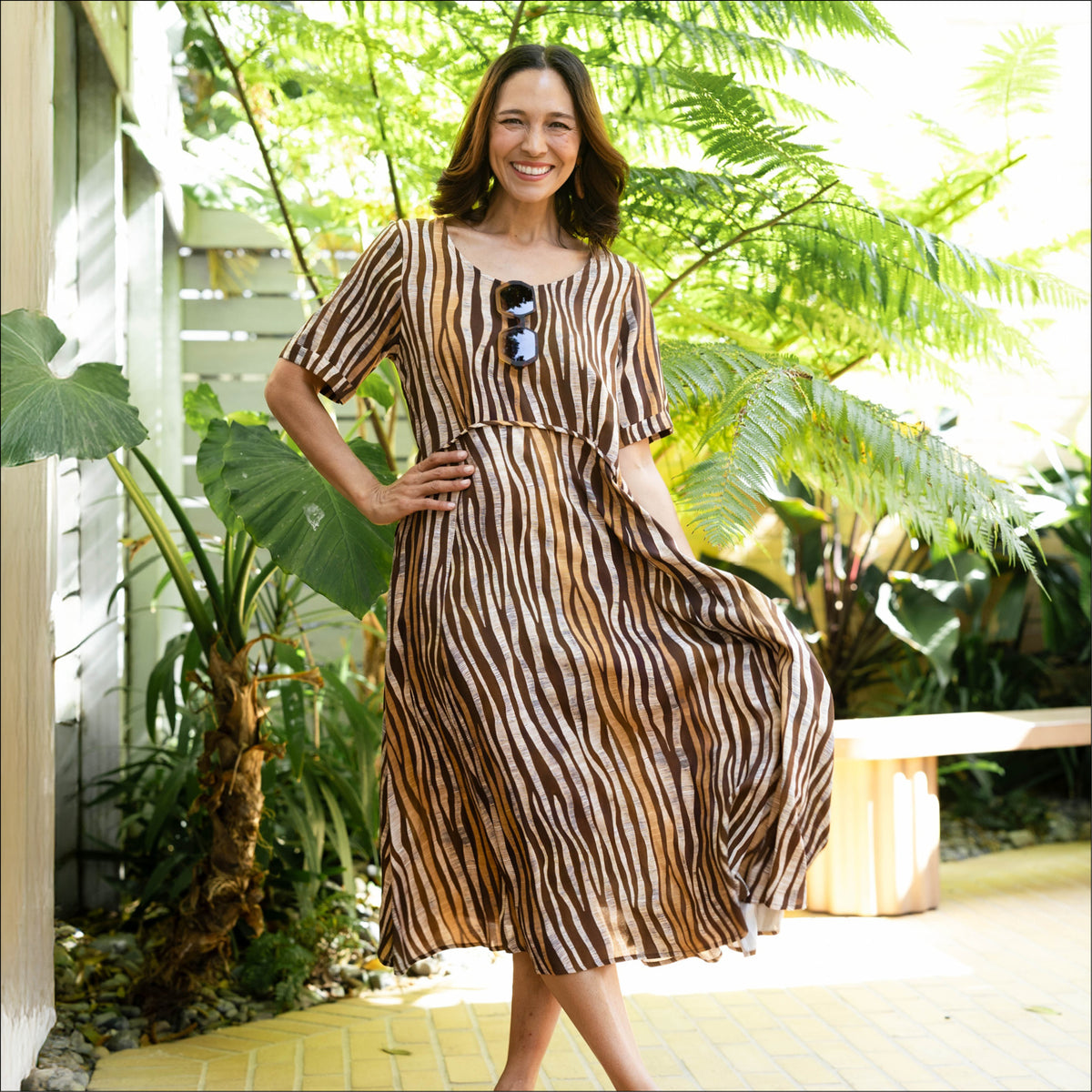 Brunette woman in a loose flowy crescent-waist animal stripe print sleeved dress, in brown and tan colours with a round neckline.