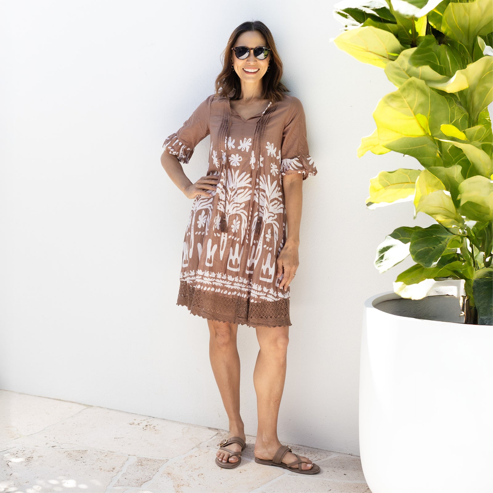 Brunette woman stands wearing a brown and white printed dress with sleeves and a skirt above the knee, suitable for petites.
