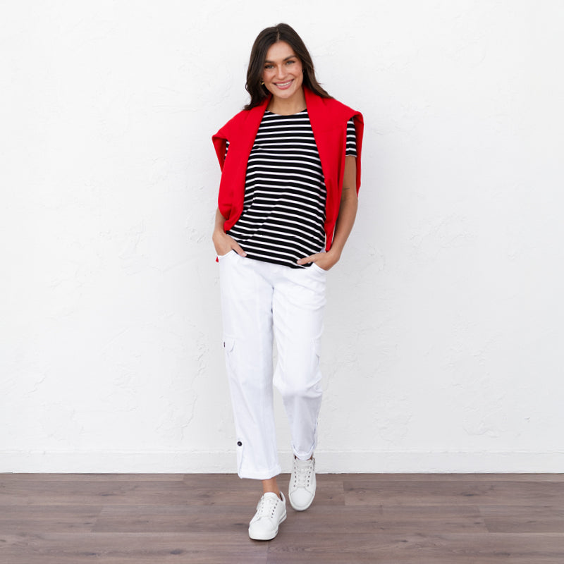 Brunette woman wearing white cargo pants and a black stripe shirt with a red sweater