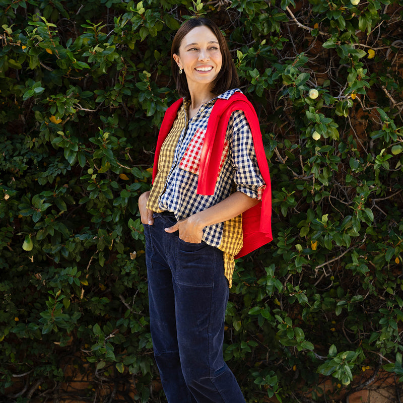 Brunette woman wearing navy blue barrel pants and a colourful check shirt with a red sweater