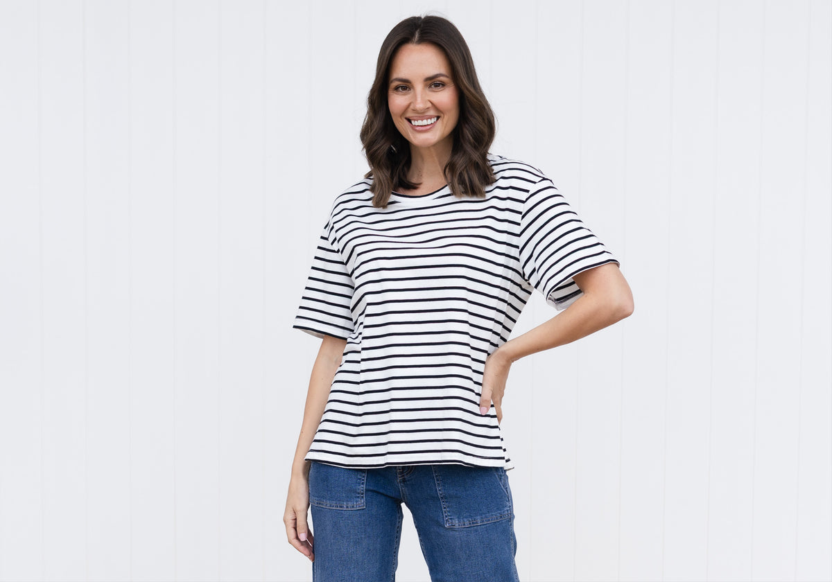 Brunette woman in boxy striped oversized T-shirt smiles and poses with a hand on her waist.