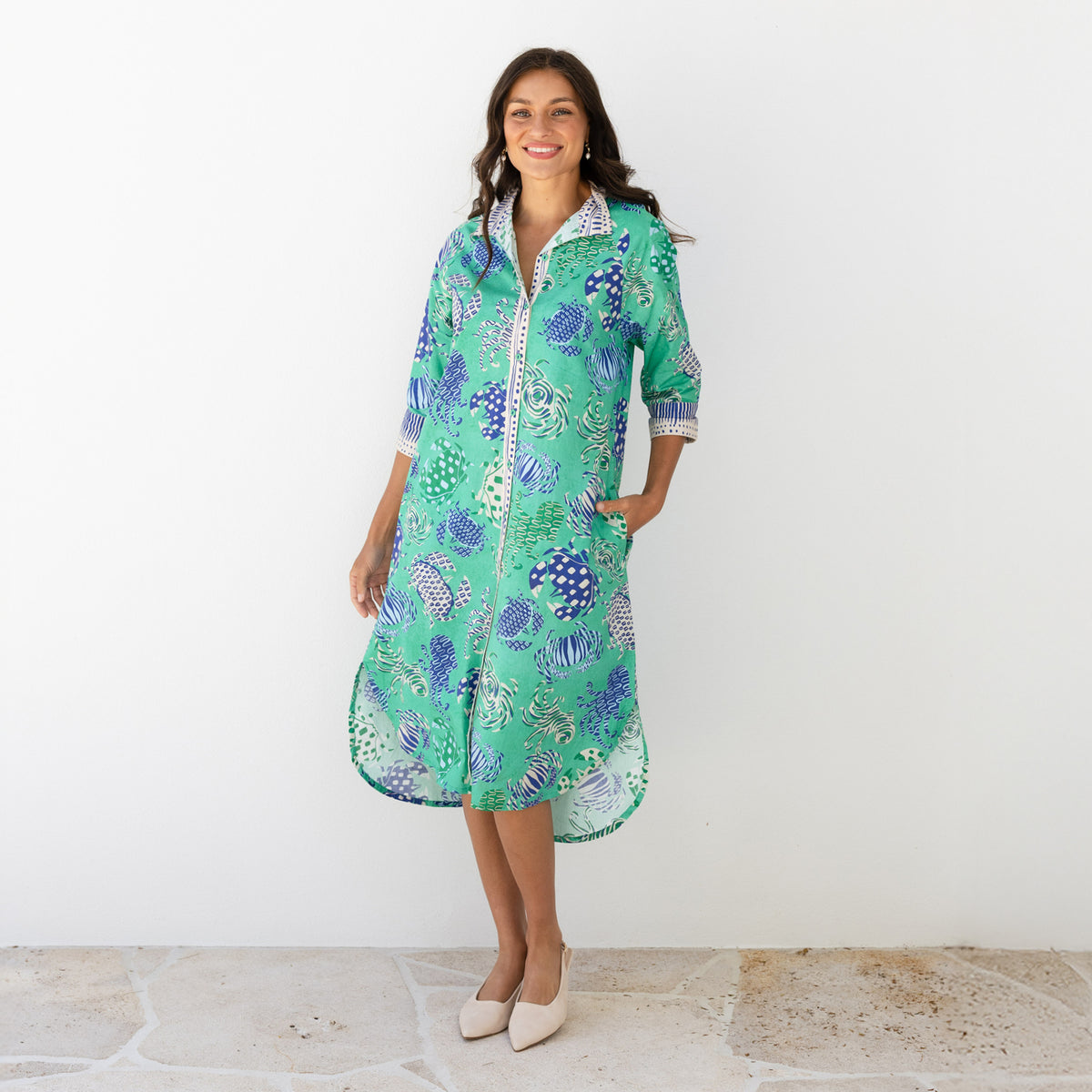 Brunette woman wearing a green shirt dress with pockets.