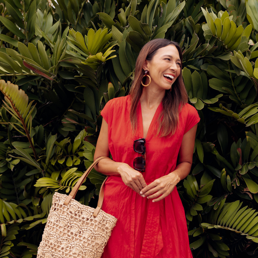 Brunette woman wearing a red Christmas Day dress in front of a garden.