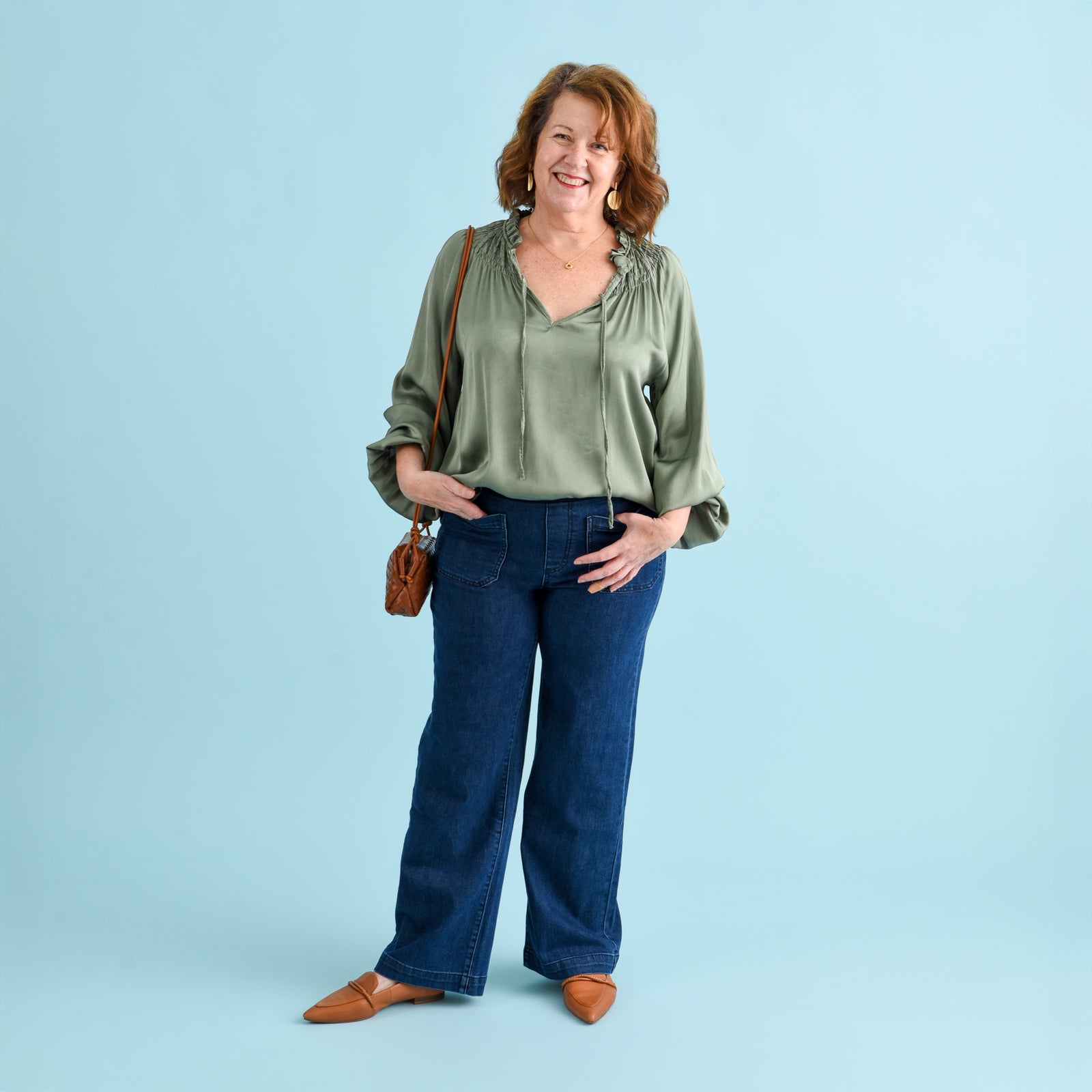 Brunette woman wearing blue denim jeans and a sage green blouse.