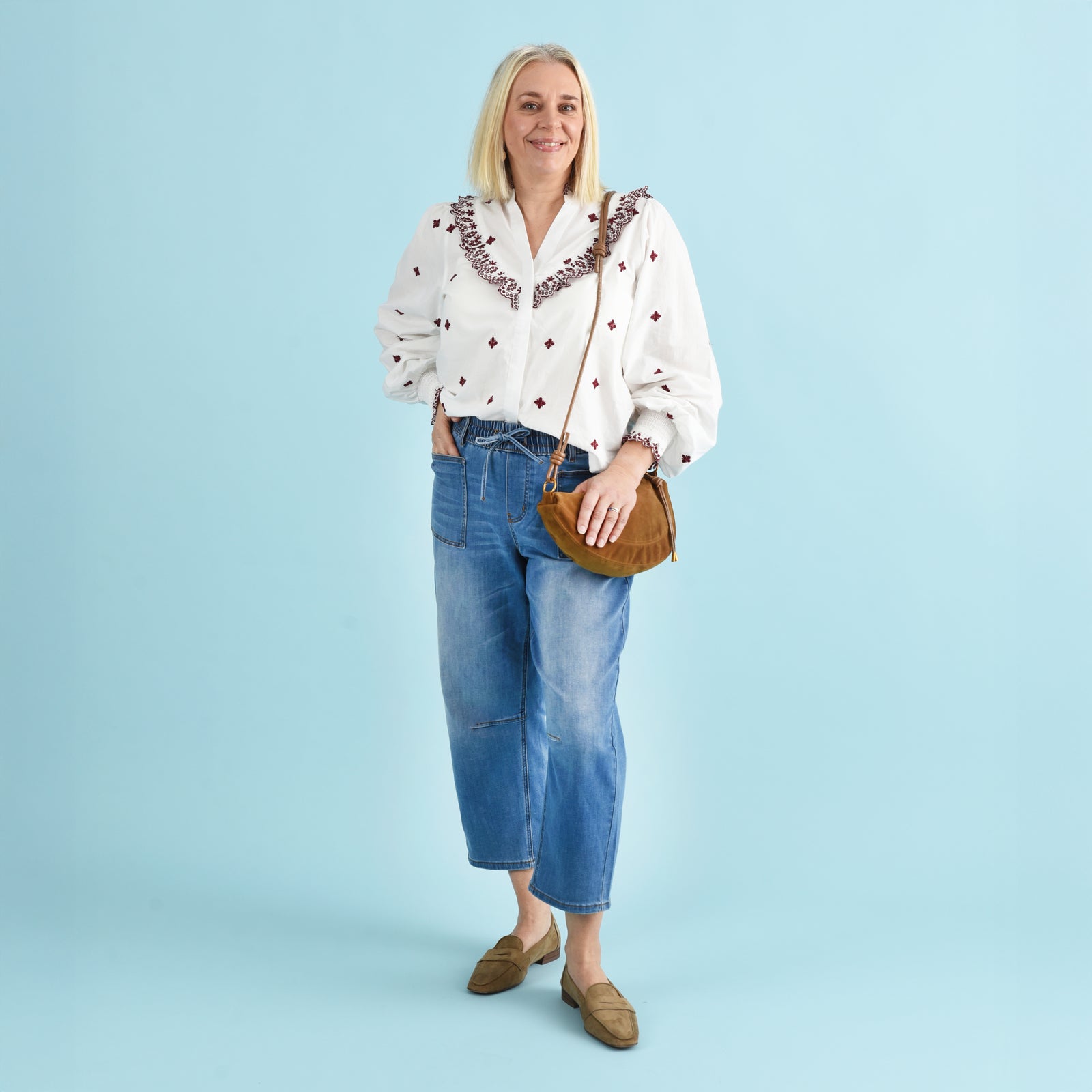 Blonde woman wearing blue denim jeans and a white and red blouse.