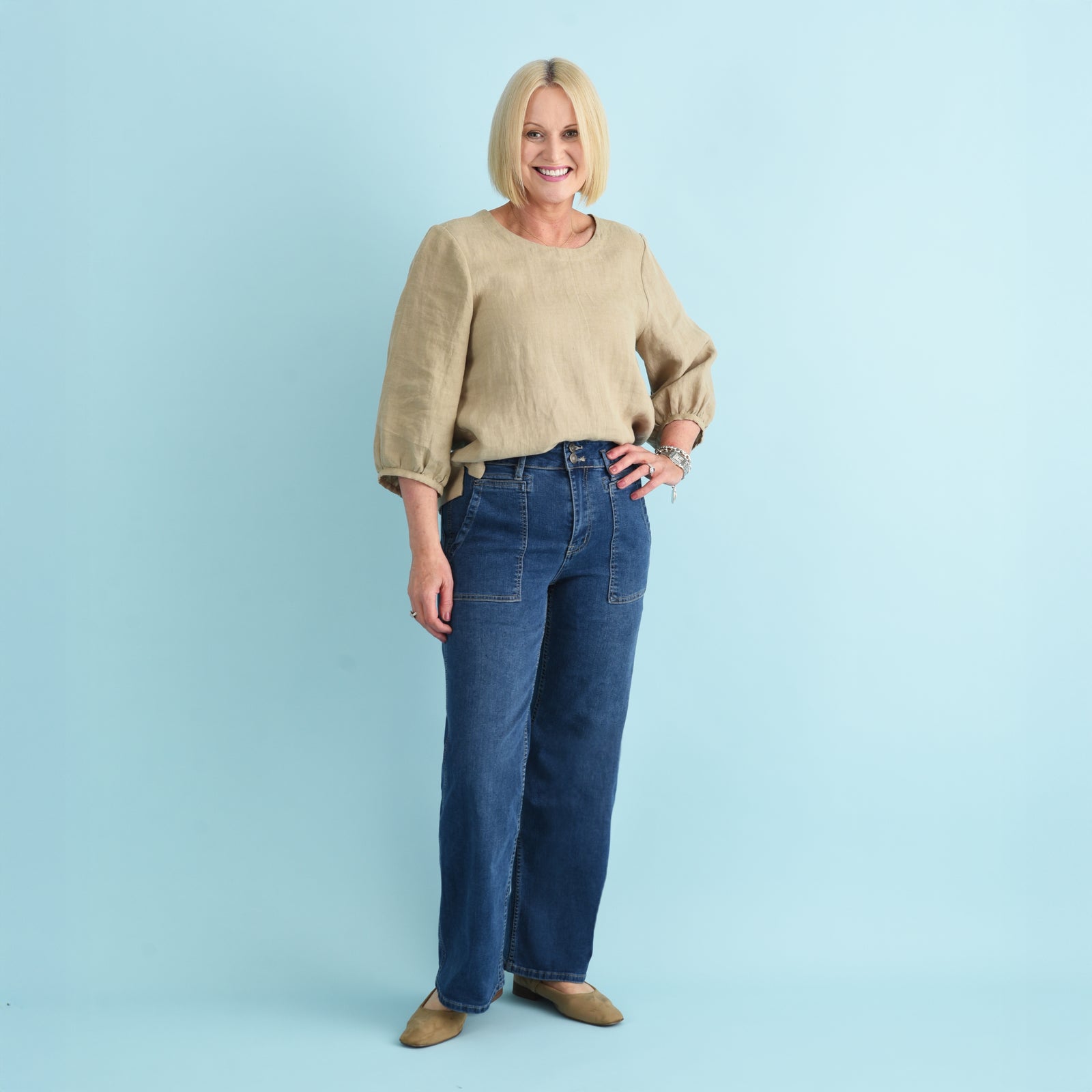 Blonde woman wearing blue denim jeans and a beige linen top.