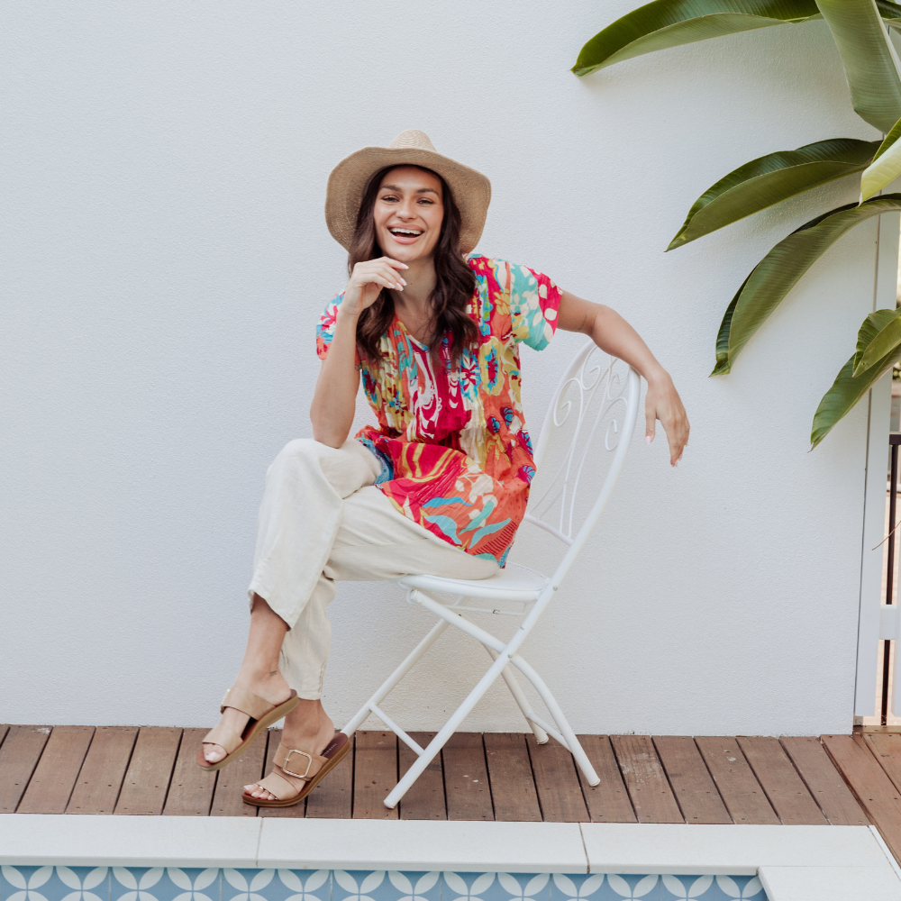 Brunette women sitting in a colourful outfit next to a pool.