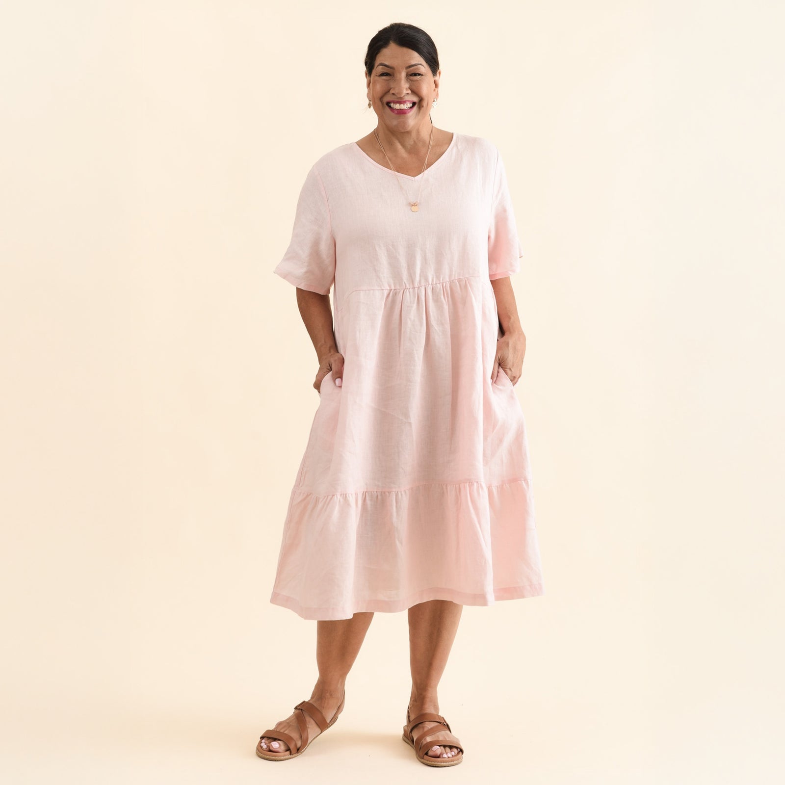 Brunette woman wearing a blush linen midi dress with half sleeves and a V-neckline, with flat tan sandals.