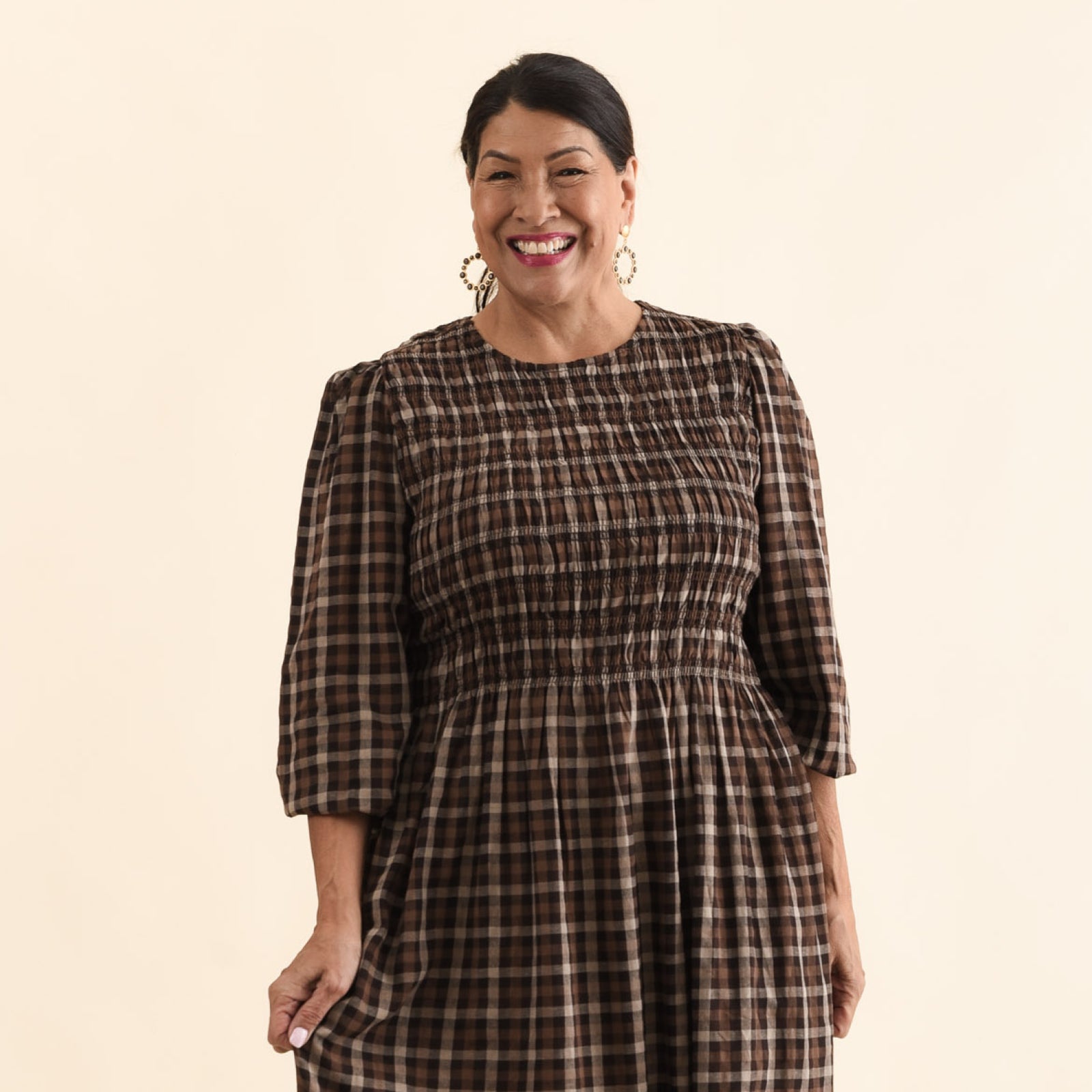 Brunette woman wearing a brown check dress with round neckline, shirred bust detail and three quarter sleeves.