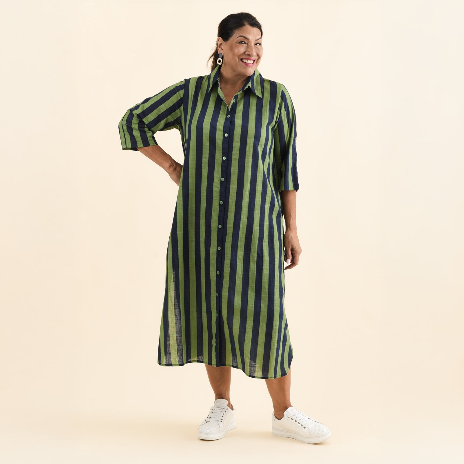 Brunette woman wearing a green striped midi shirt dress and white sneakers. 