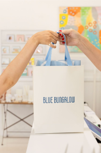 Person holding a blue tote bag with 'Blue Bungalow' branding in a store setting.