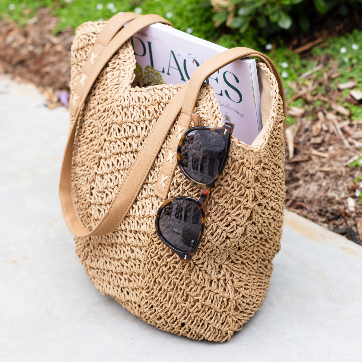 Woven travel bag holding sunglasses and a magazine on a garden ledge.